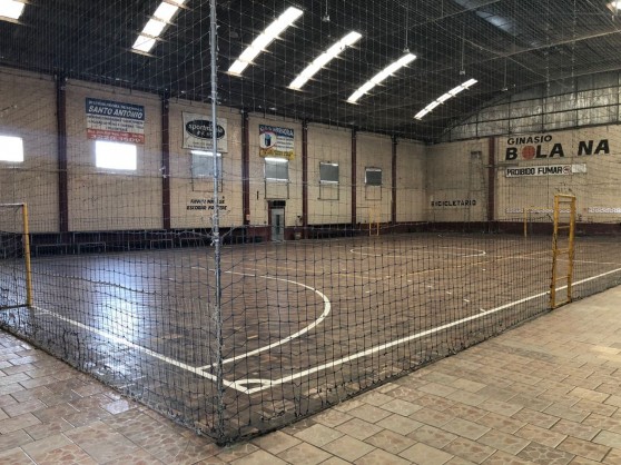 Quadra de futsal vazia, com o nome do ginásio pintado na parede de tijolo
